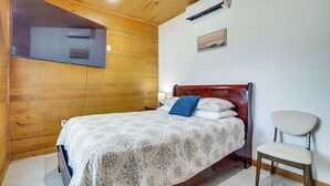A wooden-paneled room with a bed, a chair, and a mounted air conditioner.
