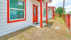 A row of single-story houses with red-framed windows and doors, a gravel driveway, and a wooden fence.