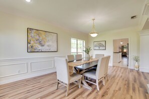 Un comedor con una mesa de madera, sillas tapizadas blancas y un mantel tejido.