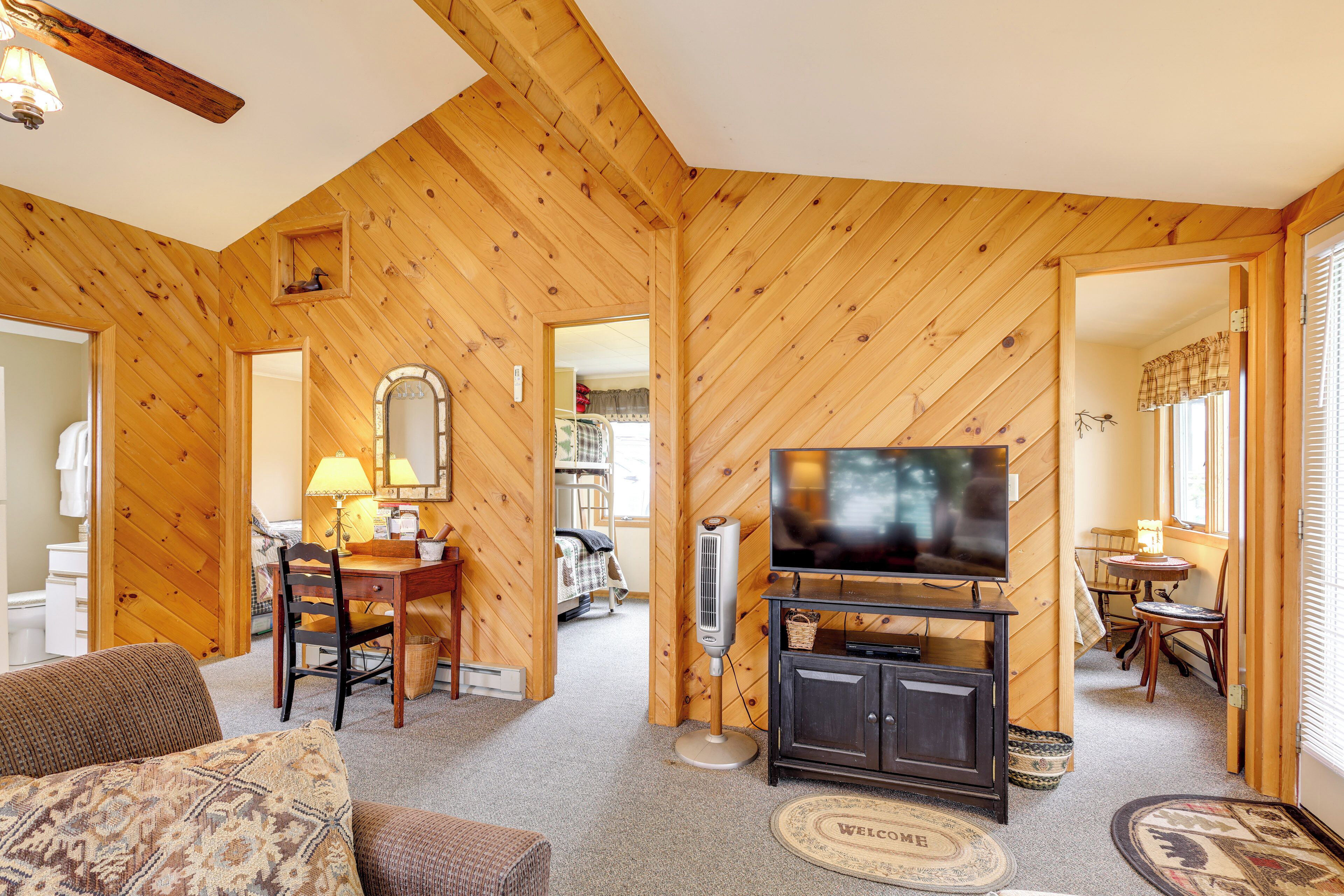 Ein gemütliches Zimmer mit Holzwänden, einem Fernseher auf einer Kommode, einem Esstisch mit Stühlen und einem Sofa.