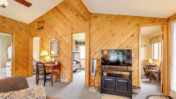 Ein gemütliches Zimmer mit Holzwänden, einem Fernseher auf einer Kommode, einem Esstisch mit Stühlen und einem Sofa.