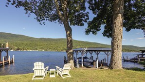 A lakeside deck with Adirondack chairs, a gazebo, and a dock extending into the water. - Waterfront Cottage on Lake George w/ 2 Docks! (Queensbury)