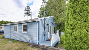 A single-story blue mobile home with a porch and a small deck, surrounded by a well-maintained lawn and a tall evergreen tree. - Waterfront Cottage on Lake George w/ 2 Docks! (Queensbury)