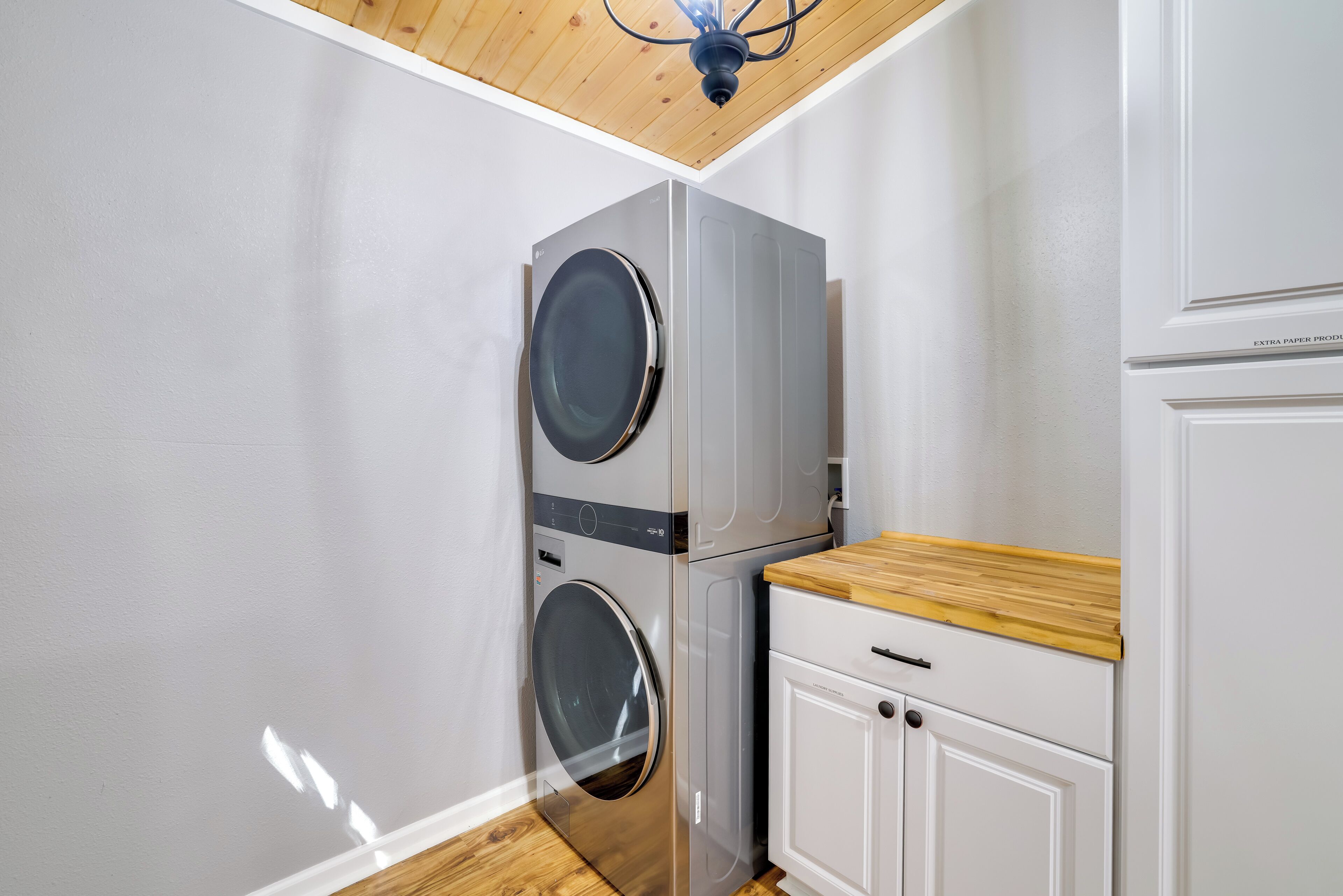 A laundry room with two stacked washing machines, a wooden countertop, and a cabinet labeled 'Laundry Supplies'.