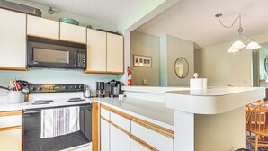 Una cocina con armarios blancos, microondas, estufa y cafetera.