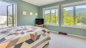 Un dormitorio con una cama grande, televisor y vistas a un bosque a través de amplias ventanas.
