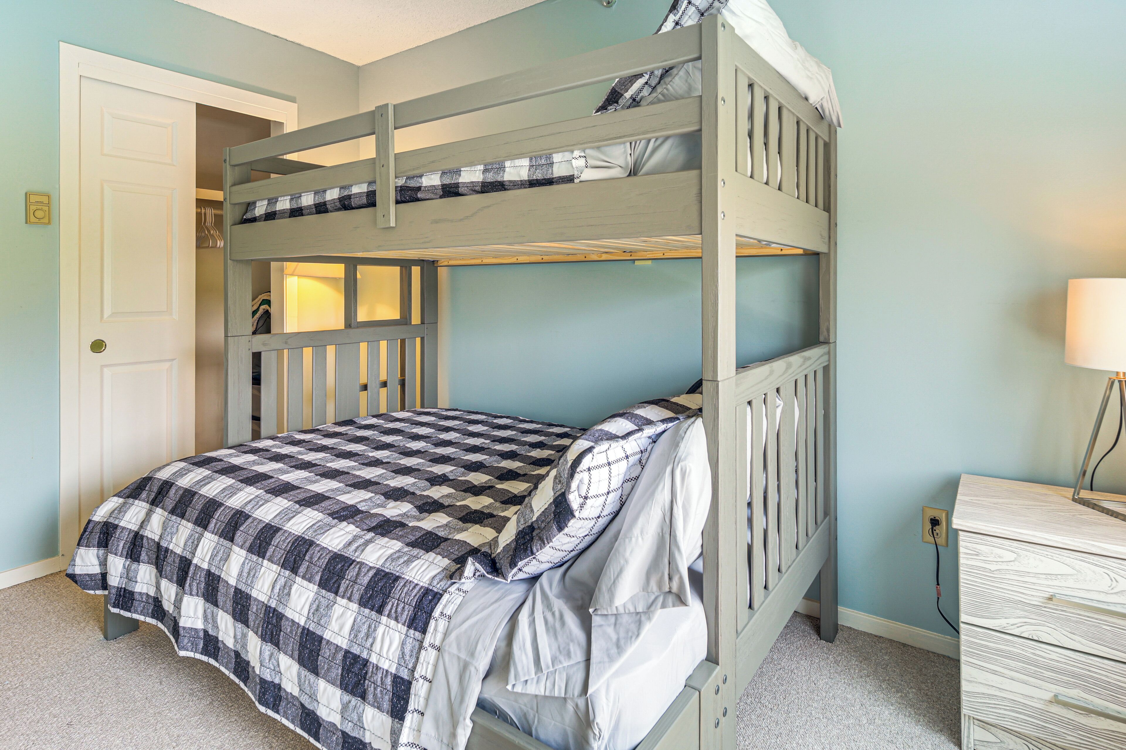 A bunk bed with a checkered bedspread, a dresser, and a door in a room with light blue walls.