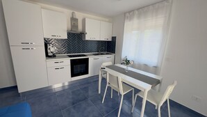 Una cocina moderna con gabinetes blancos, salpicadero de baldosas negras y un comedor con mesa y sillas.