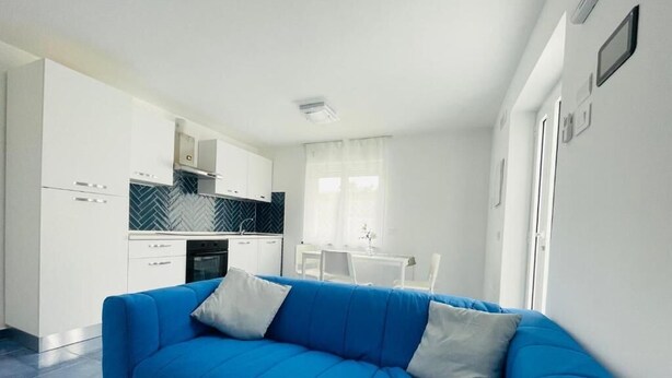 Una cocina moderna con armarios blancos, un sofá azul y un comedor con mesa y sillas blancas.
