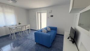 Una habitación moderna y luminosa con un sofá azul, una mesa de comedor con sillas y un televisor sobre un mueble.