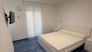 Un dormitorio con cama, mesita de noche, televisión montada en la pared y ventana con vistas.