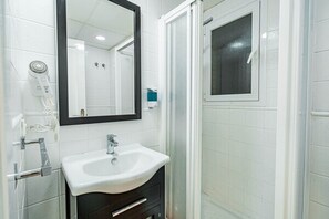 Un bany amb un lavabo blanc, un mirall, un assecador d'eixugat i una dutxa.