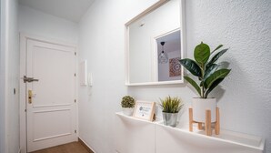 A hallway with a white door, a white wall, and a shelf with plants and a framed sign.