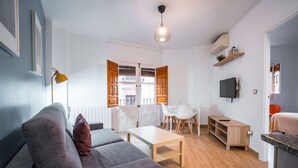 A living room with a sofa, a coffee table, a TV, and a dining area with chairs and a table. - QH Granada Center 13 (Granada)