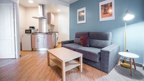 A compact living space with a kitchenette, a grey sofa, a small table, and a floor lamp. - QH Granada Center 13 (Granada)