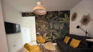 Ein modernes Wohnzimmer mit einem schwarzen Sofa, gelben Sesseln, einem Holztisch, einem an der Wand montierten Fernseher und tropischem Wandpapier.