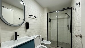 Ein modernes Badezimmer mit weiß gefliester Wand, einem runden Spiegel, einer weißen Toilette, einem Bidet und einer Duschkabine aus Glas.