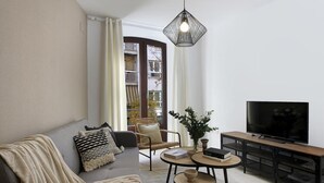 A living room with a sofa, two round tables, a TV, and a hanging light fixture. - Quality Homes Granada - QH San Juan de Dios (Granada)