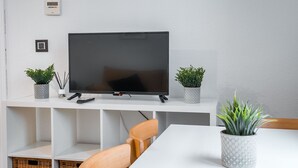 A modern living room with a flat-screen TV on a white stand, two potted plants, a remote control, and a wooden chair. - Quality Homes Granada - QH Ayuntamiento 02 (Granada)