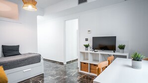 A modern living room with a sofa, a dining table, a TV, and a fireplace. - Quality Homes Granada - QH Ayuntamiento 02 (Granada)
