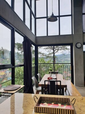Un comedor con una mesa y sillas, ventanas amplias, una lámpara colgante y vistas a un paisaje verde.