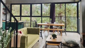 Une pièce spacieuse avec de grandes fenêtres, un canapé vert, une table en bois et un escalier.