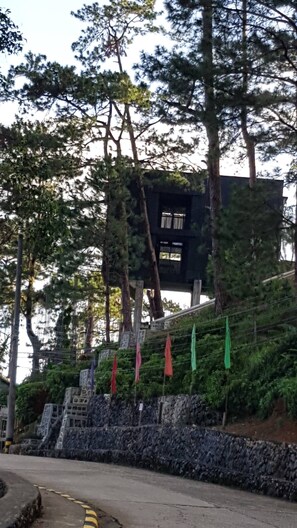 Un edificio con techo inclinado, rodeado de árboles y un muro de piedra.