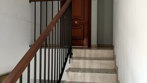 A staircase with a wooden handrail and black balusters, leading to a wooden door with a number plate. - Quality Homes Granada - QH Elvira 03 (Granada)