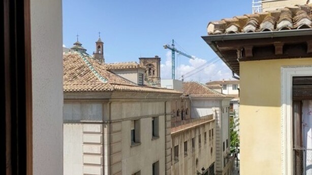 A street view with buildings, a clear sky, and a construction crane in the distance. - Quality Homes Granada - QH Elvira 03 (Granada)