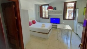 A bedroom with a bed, a TV, and a small desk area. - Quality Homes Granada - QH Elvira 03 (Granada)