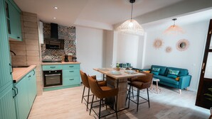 A modern kitchen with teal cabinetry, a wooden countertop, and a dining area with a table and chairs. - QH Calderería Vieja (Granada)
