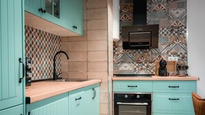 A kitchen with teal cabinets, a patterned backsplash, and a built-in oven. - QH Calderería Vieja (Granada)