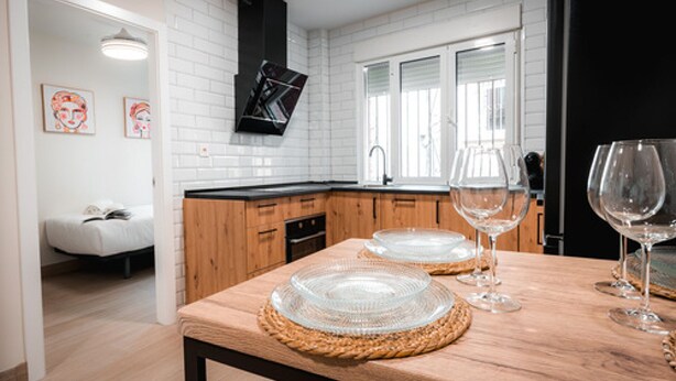 A modern kitchen with white subway tiles, wooden cabinets, and a black range hood. There are two wine glasses on the counter. - QH Hornillo de Cartuja (Granada)
