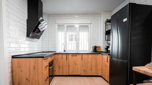 A modern kitchen with wooden cabinets, a black refrigerator, and a window with blinds. - QH Hornillo de Cartuja (Granada)