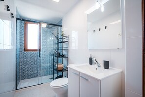 Ein modernes Badezimmer mit Duschkabine aus Glas, einem weißen Waschbecken mit Spiegel darüber und einer Toilette.