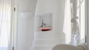 A white room with a fireplace, a white armchair, and a small shelf with a ship model.