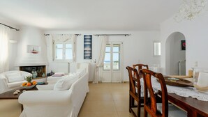 A spacious living room with a fireplace, white furniture, and a dining area with wooden chairs and a table.