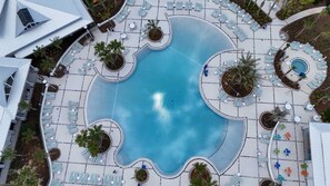 Vue aérienne d’un complexe hôtelier doté d’une piscine centrale, entourée de transats et de palmiers.