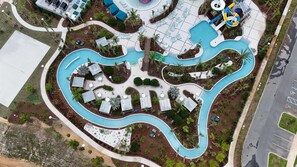 Vista aérea de un complejo turístico con una piscina serpenteante, varias zonas de descanso y un tobogán de agua.
