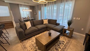 A modern living room with a sectional sofa, a wooden coffee table, and a patterned rug. - Magical 5BR w Pool Minutes From Disney 16161 (Clermont)