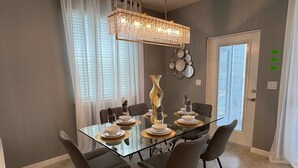 A modern dining room with a glass table, six chairs, a chandelier, and a decorative vase. - Magical 5BR w Pool Minutes From Disney 16161 (Clermont)
