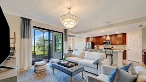 A modern living room with a sofa, ottoman, and a chandelier. - Golf Course Townhome Resort Amenities 2B Luxury (Bradenton)