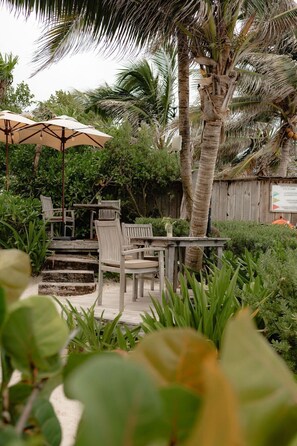 A patio area with a wooden table and chairs, surrounded by lush greenery and palm trees. - Hidden Gem With Private Pool and Rooftop Terrace (Tulum)
