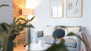 A modern living room with a grey sofa, a round coffee table, and a lamp. There are two framed artworks on the wall. - Quality Homes Granada - QH Correo Viejo 03 (Granada)