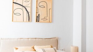 A neatly made bed with white linens and two decorative pillows, a bedside lamp, and abstract wall art. - Quality Homes Granada - QH Correo Viejo 03 (Granada)