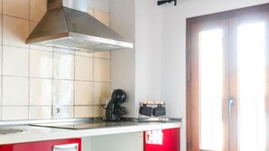 A kitchen with a red cabinet, a stainless steel range hood, and a window with wooden frames. - Quality Homes Granada - QH Correo Viejo 03 (Granada)