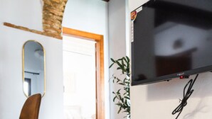 A modern living room with a wooden bench, a flat-screen TV mounted on the wall, and a mirror on the wall. - Quality Homes Granada - QH Correo Viejo 03 (Granada)