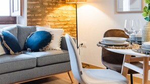 A cozy living room with a grey sofa, a wooden dining table set with plates and glasses, and a brick wall. - Quality Homes Granada - QH Correo Viejo 04 (Granada)