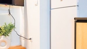 A kitchen with a white refrigerator, a wooden cabinet, and a wall-mounted television. - Quality Homes Granada - QH Correo Viejo 04 (Granada)