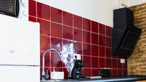 A kitchen with a red tiled backsplash, a white refrigerator, a black coffee machine, and wooden cabinets. - Quality Homes Granada - QH Correo Viejo 04 (Granada)
